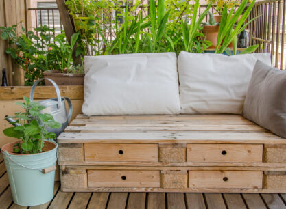 drewniane siedzisko z palet z poduszkami, w tle zielone trawy ozdobne, obok doniczka miętowa z miętą
