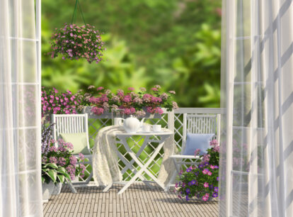 widok na balkon z białymi meblami, różowymi i fioletowymi kwiatami